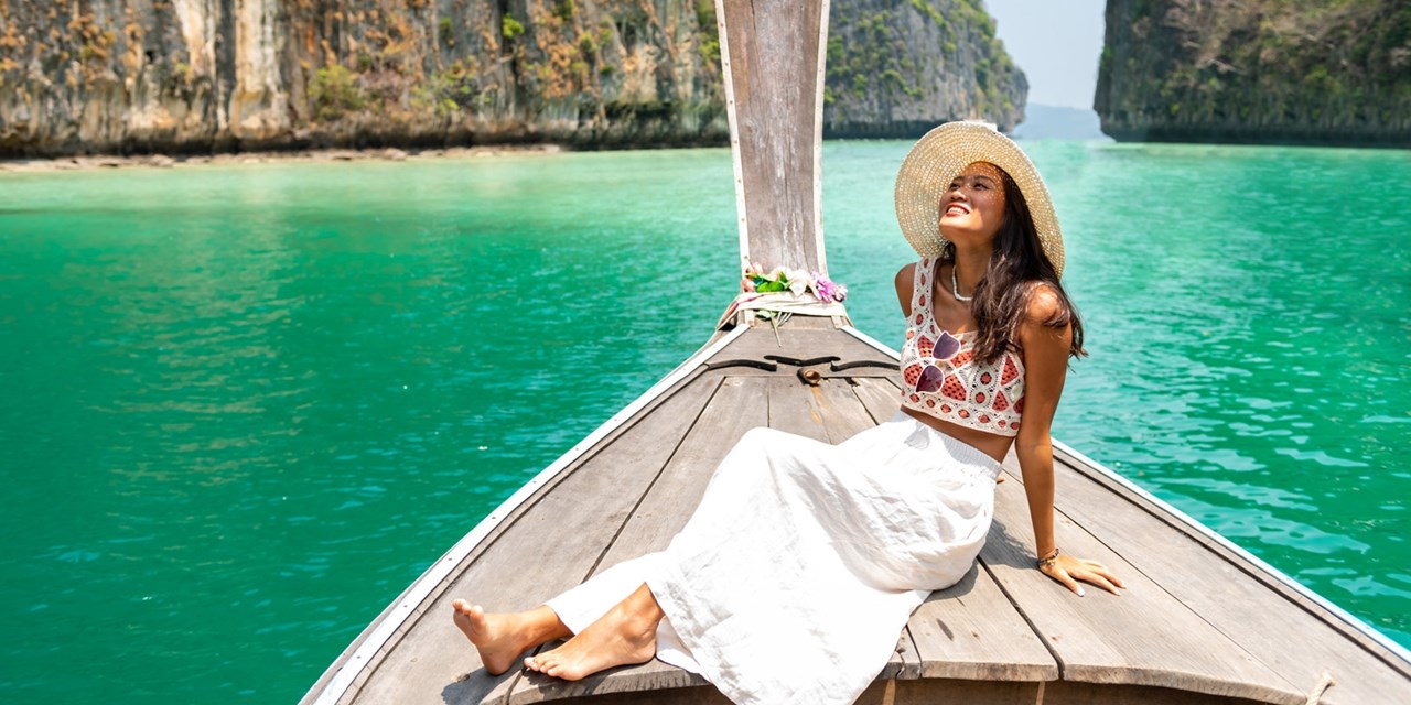 A woman rides the bow of a longtail boat past limestone cliffs in Krabi