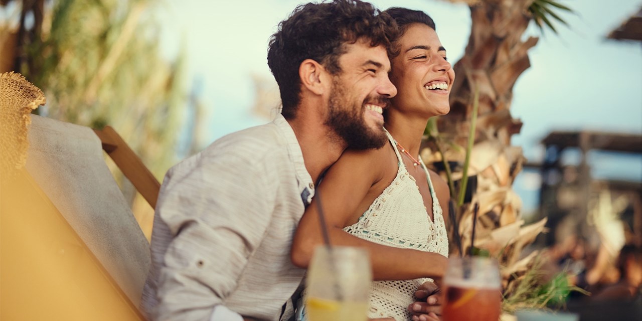 A couple relaxes with drinks at an outdoor beach bar at sunset