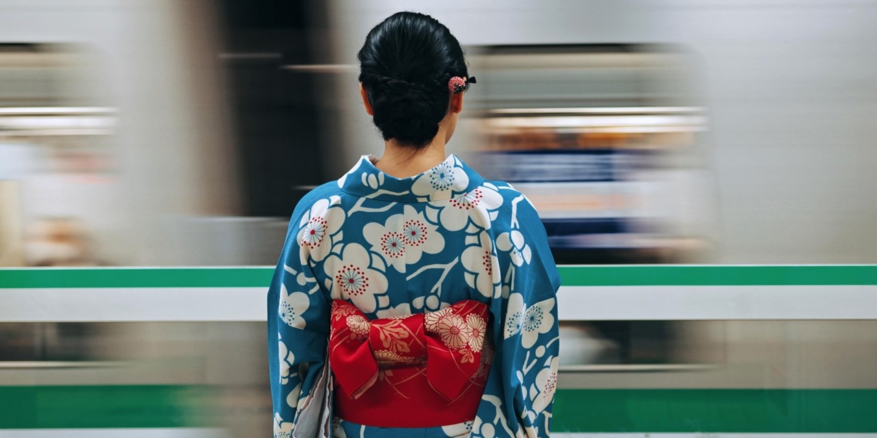 A Japanese woman wearing a traditional blue kimono waits for the next train on a Tokyo subway platform