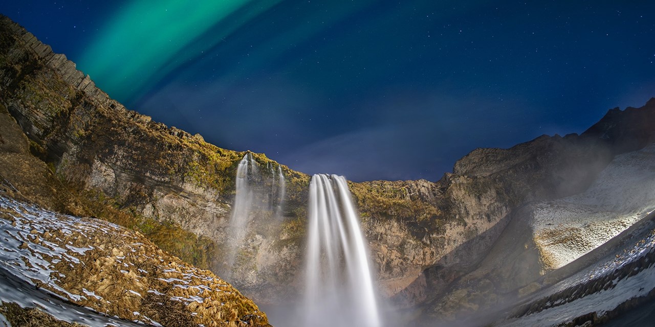 Seljalandsfoss waterfall beneath a green aurora borealis