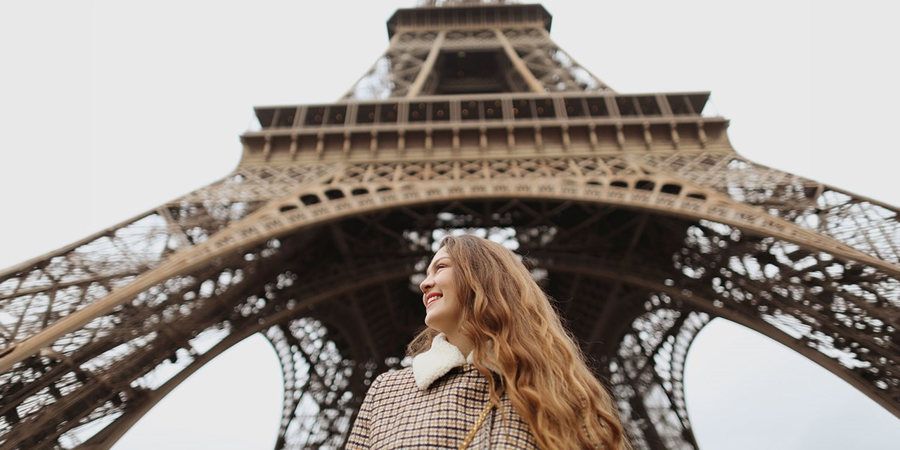 A visitor smiles beneath the arches of the Eiffel Tower in Paris