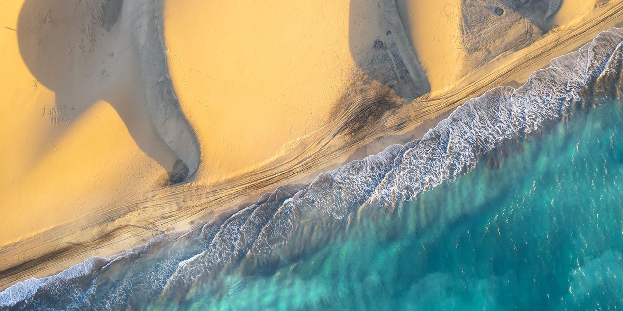 Desde lo alto, las Dunas de Maspalomas se aprecian como un mar de arena dorada que se extiende hasta el océano Atlántico