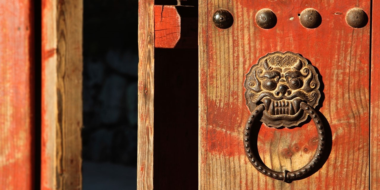 A lion head knocker hangs on a weathered red door in Gyeongju